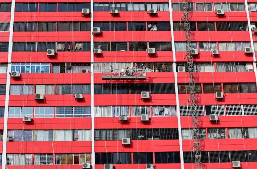 Red building facade in Singapore with workers on suspended platform, day.